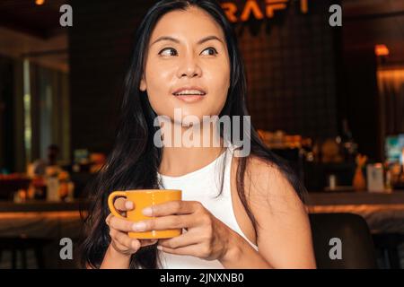 Donna asiatica sorridente che beve un caffè in un ristorante o in una caffetteria Foto Stock