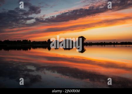 Nuvole colorate riflesse nell'acqua del lago dopo il tramonto Foto Stock