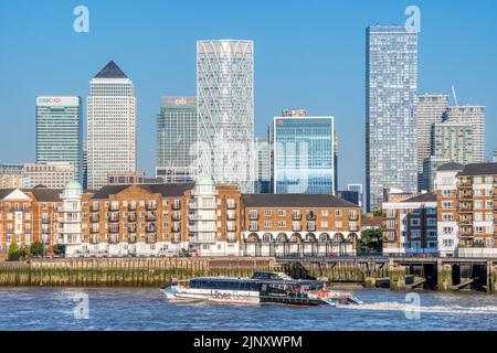 Una barca Uber da Thames Clippers passando la Penisola di Rotherhithe con Canary Wharf e l'Isola dei cani sullo sfondo. Foto Stock