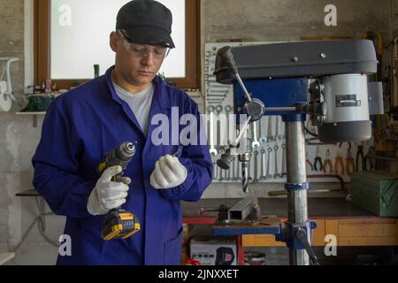 Immagine di un fabbro nella sua bottega che tiene un trapano e una punta rotta. Fatelo da soli e il duro problema della lavorazione dei metalli Foto Stock