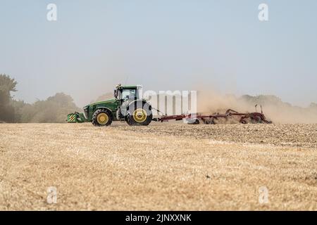 Un trattore aratri un campo durante una siccità in Norfolk come raccolti asciugano fuori e tubo flessibile e divieti di irrigazione sono imposti, Norfolk, Gran Bretagna. Foto Stock