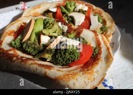 appetitosi pancake vegetariani con broccoli e pomodoro rosso e fette di formaggio si posano sul piatto per cena Foto Stock