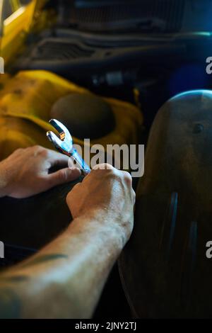 Mani di giovane tecnico muscolare o riparatore con chiave metallica in piedi davanti al motore di auto mentre andando a riparare i suoi dettagli Foto Stock