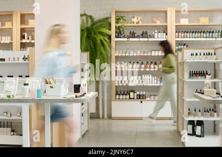 Movimento sfocato di due giovani donne che si muovono insieme a display con articoli per la cura del corpo, cura della pelle, nailcare e prodotti per il trucco Foto Stock