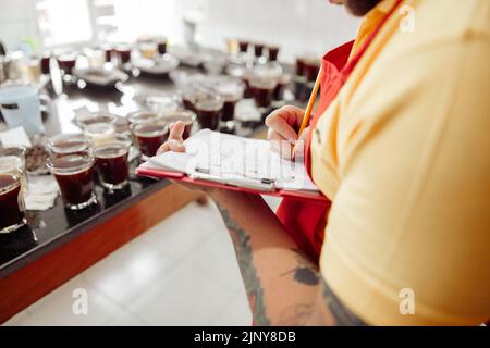 Foto ritagliata dell'uomo che prende appunti durante la degustazione del caffè Foto Stock