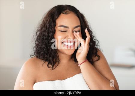 Naturale bellezza essenziale. Donna allegra nera più taglia con gli occhi chiusi che toccano la sua morbida pelle impeccabile, ridendo Foto Stock