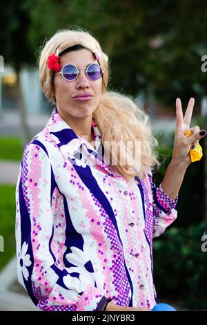 Donna che fa un gesto mano segno V e indossa un costume da hippie a una festa di Halloween a Fountain Hills, Arizona. Foto Stock