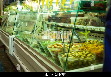 Olive in vendita da unità refrigerata in uno stand di prodotti alimentari mediterranei nel mercato cittadino di Cardiff (Regno Unito) Foto Stock