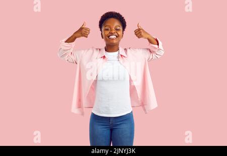 Gioioso eccitato giovane afroamericana che mostra i pollici in su che raccomanda il prodotto di pubblicità. Foto Stock