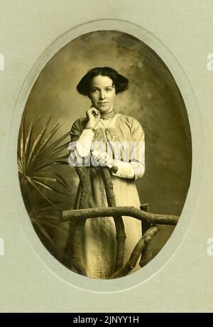 Vintage 20th ° secolo Fotografia Studio Ritratto prendere di giovane donna in piedi e indossare abiti bohémien elegante del periodo circa 1916 Foto Stock