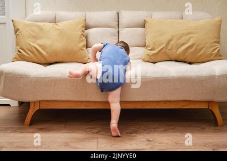 Il bambino sale sul divano. Bambino che impara a scendere dal letto. Bambino di un anno Foto Stock