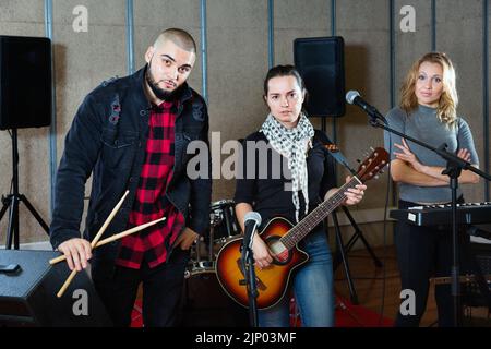 Tre bandmates che si posano insieme a strumenti musicali nella sala delle prove Foto Stock