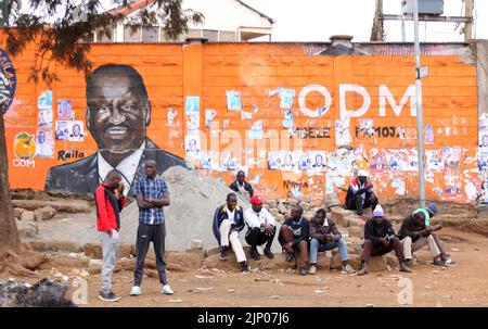 La gente siede intorno al murale del frontone presidenziale Raila Odinga a Kibera. La vita quotidiana come il paese attende i risultati elettrici. Il Kenya ha vissuto in passato una violenza post-sondaggio. L'organo elettorale IEBC di Nairobi sta attualmente ottenendo risultati con un periodo di sette giorni per annunciare i risultati che scadono martedì 16th agosto 2022. Il corpo indicava un lento processo di tallying. Foto Stock