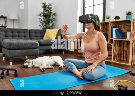 Giovane donna sorridente allenata con sicurezza utilizzando occhiali per realtà virtuale a casa Foto Stock