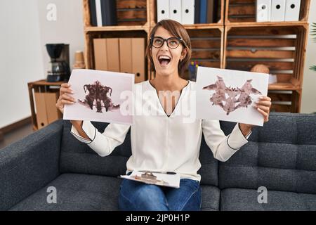 Brunette donna che lavora con rorschach test in psicologia clinica arrabbiato e pazzo urlando frustrato e furioso, urlando con rabbia cercando in su. Foto Stock