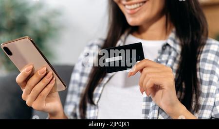 Primo piano dello smartphone e della carta bancaria nelle mani di una donna. Shopping online. Felice donna fa acquisti su Internet, tiene un telefono cellulare e una carta di credito, paga per le merci online, sorridendo Foto Stock