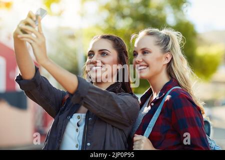 Scattiamo delle foto per dare un'occhiata alle nostre esperienze. Due belle amiche scattano un selfie in città. Foto Stock