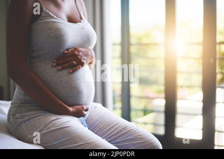 Con una pancia crescente viene un legame crescente. Una giovane donna incinta che si rilassa sul letto a casa. Foto Stock