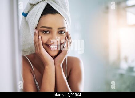 La pelle nutrita si illuminerà naturalmente. Ritratto di una giovane donna attraente che guarda il suo volto nello specchio del bagno. Foto Stock