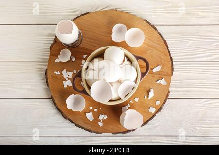 Tavola con gusci d'uovo rotti in pentola di cottura su fondo di legno bianco Foto Stock