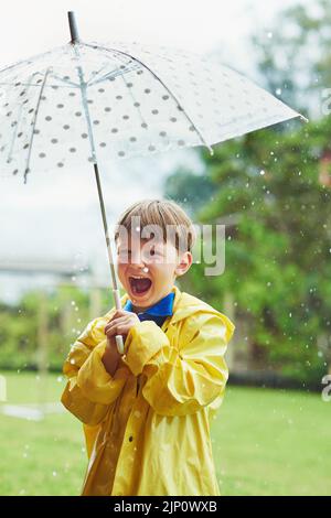 La pioggia lo rende così felice. Ritratto di un allegro ragazzino in piedi con un ombrello all'esterno in una giornata di pioggia. Foto Stock