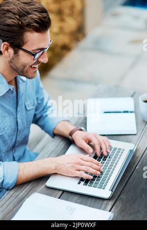 HES un blogger occupato. Un bel giovane uomo che usa un computer portatile all'aperto. Foto Stock