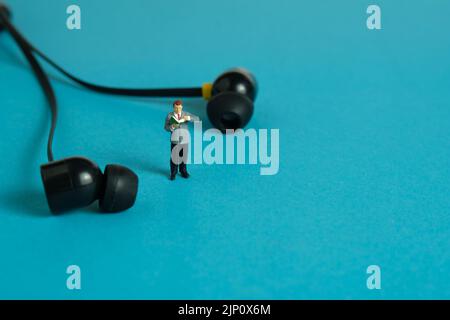 Fotografia di figura giocattolo delle persone in miniatura. Uno studente maschile che si rilassa, in piedi leggendo un libro mentre ascolta la musica. Foto dell'immagine Foto Stock