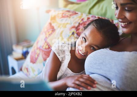 Andavano solo a rilassarsi oggi. Ritratto di una adorabile bambina che si rilassa con la madre mentre la legge una storia a casa. Foto Stock