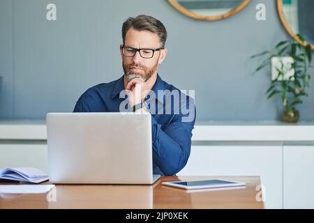 Lavorare a casa. Un uomo di mezza età concentrato che lavora sul suo notebook mentre si contempla a casa durante il giorno. Foto Stock
