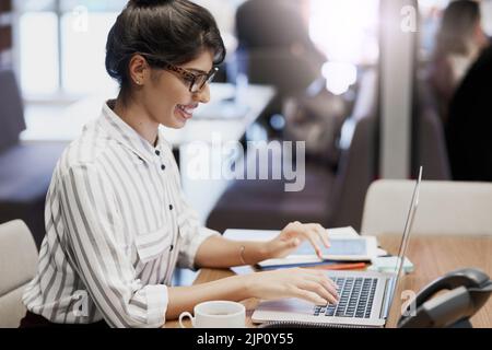 Lavora sodo per tutta la giornata di lavoro. Una giovane donna d'affari sicura che lavora su un notebook in ufficio. Foto Stock