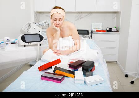 Ritratto di una donna anziana in un salone di bellezza. La donna è perplessa dalla giusta scelta dei cosmetici. Foto Stock