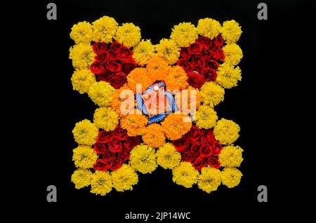 Rangoli decorativi di fiori di rosa e marigold per il festival Diwali con lampada in argilla diya illuminata con fuoco sfocato fiamma su sfondo nero. Foto Stock