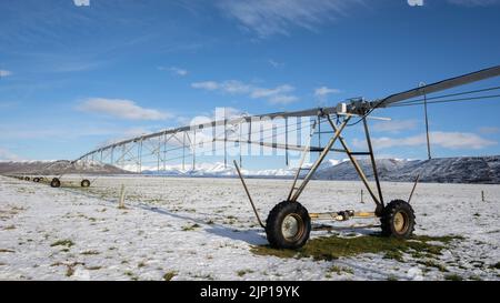 Impianto di irrigazione a sprinkler su un terreno innevato con la gamma ben Ohau sullo sfondo, Twizel, South Island. Foto Stock