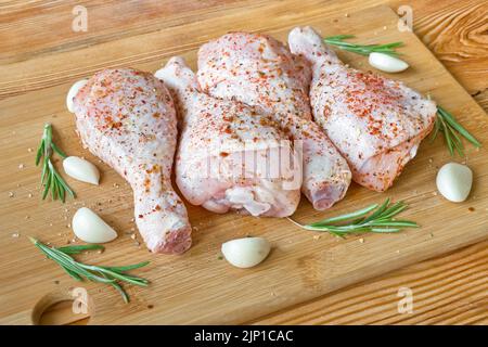 Cosce di pollo crude marinate con spezie, aglio e rosmarino su un tagliere di legno. Messa a fuoco selettiva. Foto Stock
