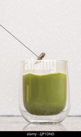 Tè verde matta latte in un bicchiere. Il latte verde opaco viene versato in un vetro trasparente con fondo doppio Foto Stock