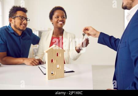 Agente immobiliare o immobiliare dà le chiavi a casa nuova per felice giovane coppia nera Foto Stock