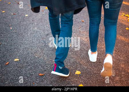 Una giovane coppia cammina in un parco con foglie cadute in un giorno d'autunno. Uomo e donna in jeans e sneakers. Foto Stock