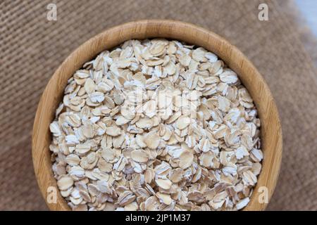 Fiocchi di avena crudi in ciotola di legno su pezzo rustico di sackcloth, concetto di cibo vegano sano mangiare. Vista dall'alto, primo piano, messa a fuoco selettiva Foto Stock