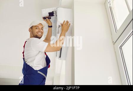 Ritratto di amichevole professionista maschio che installa nuovo condizionatore d'aria nell'appartamento del cliente Foto Stock