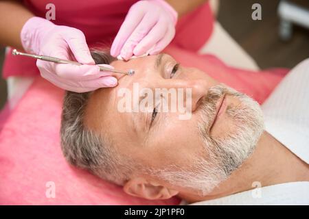 Cosmetologo con cucchiaio uno faccia pulita dell'uomo da acne Foto Stock