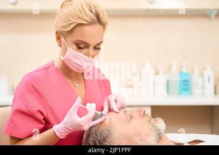 Attraente estetista femminile che dà l'iniezione di bellezza alla fronte dell'uomo Foto Stock