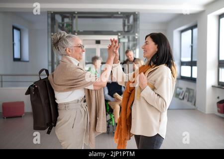 Buone donne studenti anziani che incontrano alto fiving in corridoio all'università. Foto Stock