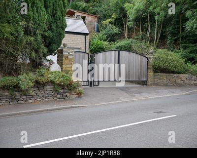 Cancelli in legno residenziali a lato della strada con assi verticali, circoschi in metallo nero con edifici e alberi sullo sfondo Foto Stock