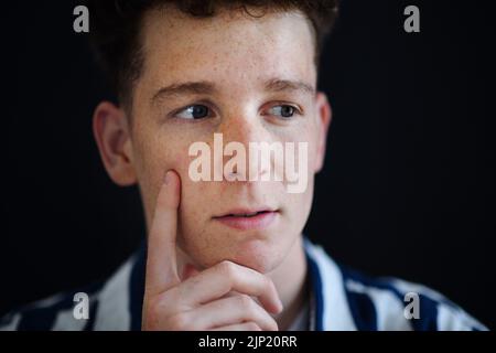 Ritratto di bel giovane uomo pensieroso con capelli zenzero e frane guardando via su sfondo nero, primo piano Foto Stock