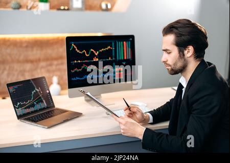 Investimenti, negoziazione in borsa. Un investitore di successo del commerciante maschio caucasico, che analizza il mercato finanziario di criptovaluta, guarda al calcolatore, che si occupa di una strategia di criptovaluta, che analizza i rischi Foto Stock