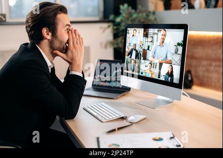 Videoconferenza in ufficio. Uomo d'affari caucasico positivo di successo in un vestito, siede in un posto di lavoro, negoziando con i partner tramite videochiamata, discutendo di nuovo progetto, termini di cooperazione Foto Stock