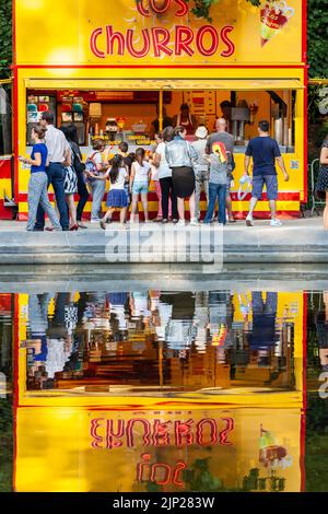 I clienti sono raggruppati di fronte a un camion alimentare che offre churros e si riflettono su un pezzo d'acqua. Foto Stock
