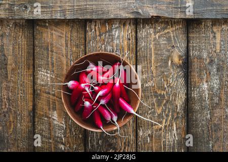 La lunga colazione si irradia in una ciotola di ceramica su un asse di legno visto dall'alto. Verdure fresche primaverili biologiche di produzione propria, cibo sano a base di piante vegane Foto Stock