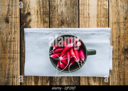 La lunga colazione si irradia in una ciotola di ceramica su un asse di legno visto dall'alto. Verdure fresche primaverili biologiche di produzione propria, cibo sano a base di piante vegane Foto Stock