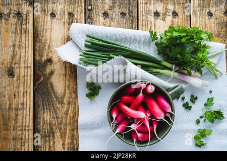 La lunga colazione irradia in una ciotola di ceramica e erbe fresche primaverili su un asse di legno visto dall'alto. Verdure biologiche, prezzemolo, primavera Foto Stock